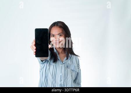 Portrait of an Indonesian woman in a blue striped shirt holding a smartphone directly toward the camera. Blurred facial expression with sharp focus on Stock Photo