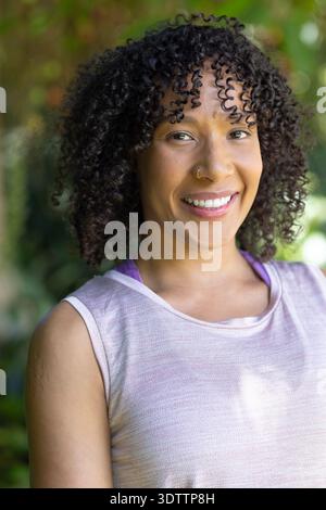 African American woman smiling and posing in park, showing nose ring, pink tank top, purple strap Stock Photo