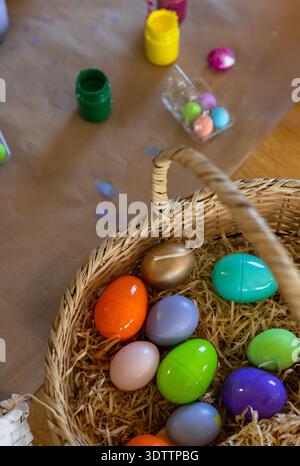 Wicker basket is sitting on kraft paper at craft table, holding colorful plastic eggs Stock Photo