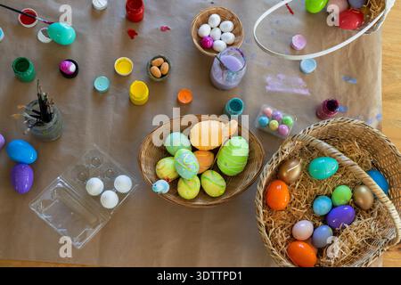 Wicker baskets holding colorful painted eggs are sitting on kraft paper table, with paint jars Stock Photo