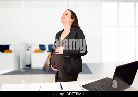 Shot of a pregnant business woman standing in her office holding her stomach and with pain Stock Photo