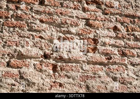 Background of an old, rugged brick wall featuring textured red bricks partially covered by a thick layer of weathered. Stock Photo