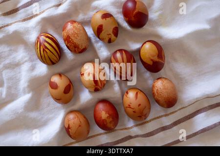 A collection of Easter eggs rests on a white cloth with brown stripes. Each egg displays unique patterns in shades of brown and reddish-orange. The de Stock Photo