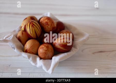 A basket filled with Easter eggs, placed on a light wooden table. The eggs are decorated in shades of brown, orange, and red with various patterns. Th Stock Photo
