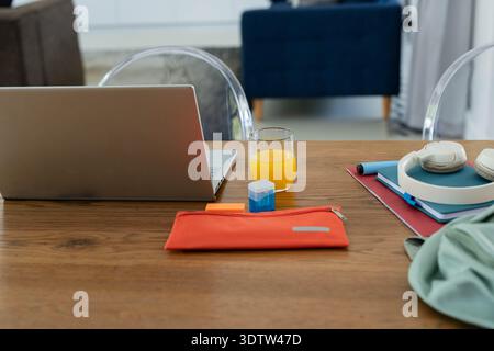 Dining table workspace showing laptop, glass of orange juice, orange pouch, notebooks, headphones Stock Photo