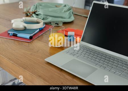 Silver laptop sitting on right of table green backpack with headphones and notebooks, copy space Stock Photo
