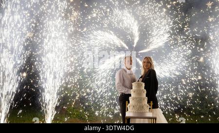 Completion of the wedding, newlyweds cutting the cake, fireworks. Newlyweds cutting a cake against the backdrop of cold lights in the evening. Cold li Stock Photo