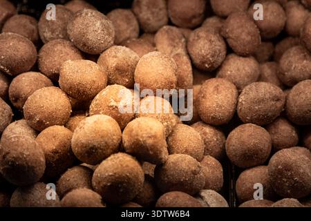 Mini donut holes coated in sugar displayed in a bakery showcase, fresh sweet pastries on sale in a pastry shop or cafe. Stock Photo