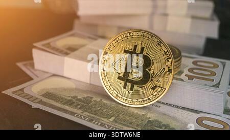 Gold bitcoin coin standing on stacks of US dollar bills, close-up finance concept with warm sunlight, cryptocurrency investment and digital money them Stock Photo