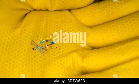 Close-up of a yellow honeycomb-textured glove holding tiny microplastic fragments and glitter, highlighting pollution and environmental contamination. Stock Photo