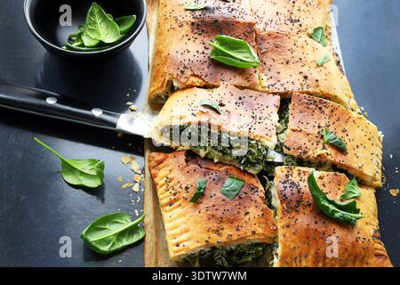 Spanakopita, a traditional Greek savory pie made with phyllo pastry, fresh spinach, and feta cheese, on a black background. Greek cuisine. Stock Photo