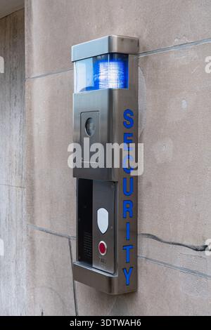 Sleek security intercom system mounted on a stone wall, featuring a stainless steel emergency call box with integrated surveillance camera, speaker Stock Photo