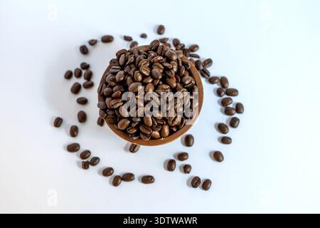 A minimalist flat lay shot of dark roasted coffee beans in a small wooden bowl, artistically arranged in a circle on a clean white surface, creating a Stock Photo