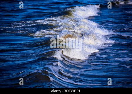 A dynamic close-up shot of a powerful ocean wave breaking, showcasing its foamy crest and turbulent white water against the deep blue surface of the s Stock Photo