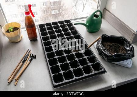 High angle view of gardening tools and empty seedling tray on a windowsill. Preparation for spring planting with fertile soil and small garden equipme Stock Photo