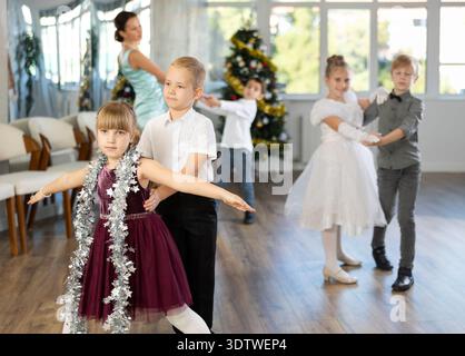 Preteen children in elegant outfits practicing partner dance in Christmas studio Stock Photo