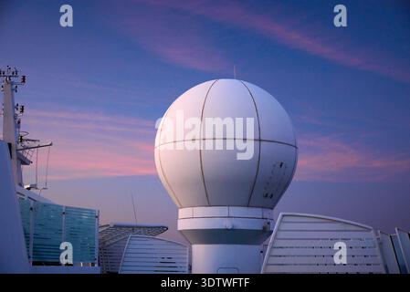 A large, white spherical radome, likely housing a radar antenna, stands prominently on a cruise ship or large vessel. It is positioned against a strik Stock Photo