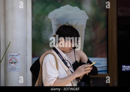 BANGKOK, THAILAND-JAN 25, 2026: Man using smartphone in outdoor market, side profile, at Chatuchak Market. Stock Photo
