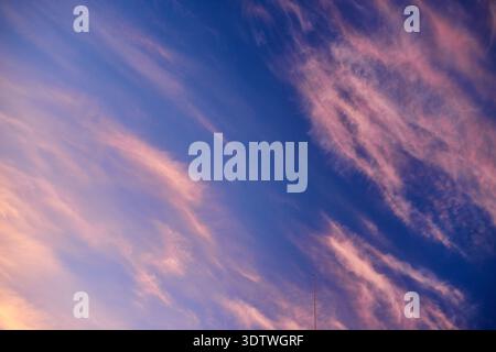 A vibrant sky at sunset or dusk, featuring a striking gradient from deep blue to purple, illuminated by soft pink and orange wisps of cirrus clouds. T Stock Photo
