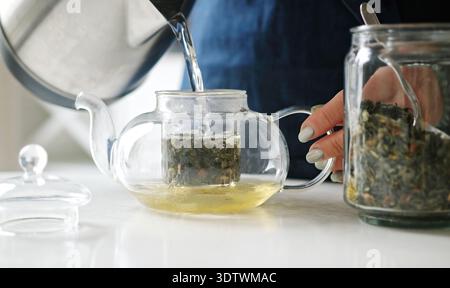 Girl In The Kitchen Filling A Teapot With Hot Water From A Kettle For Green Tea Stock Photo