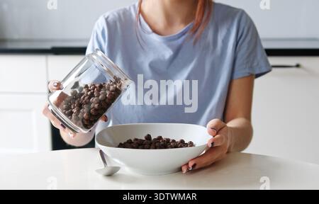 Girl Pouring Brown Cereal Balls Into A Plate For Breakfast Stock Photo