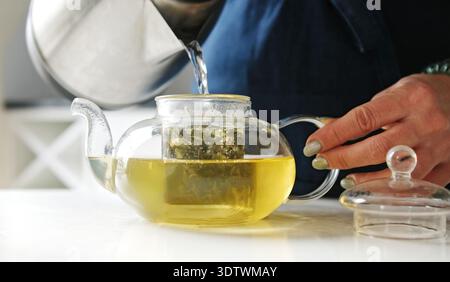 Girl In The Kitchen Filling A Teapot With Hot Water From A Kettle For Green Tea Stock Photo