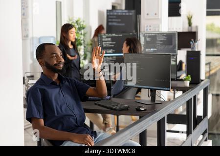 Black male software engineer interacts with invisible holographic interface, using hand gestures to explore augmented reality and futuristic digital workspace in a modern tech office. Stock Photo
