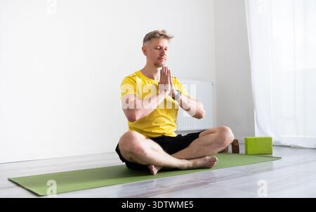 Sporty Young Man Practicing A Yoga Routine While Sitting In A Lotus Pose On A Mat Stock Photo