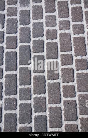 A high-angle, close-up view of a paved surface featuring rectangular, dark grey and brown interlocking pavers. The stones have irregular, slightly rou Stock Photo