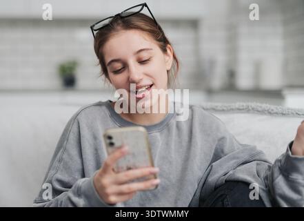 Smiling Young Woman Chatting Via Video Call While Sitting On A Sofa In A Light Room Stock Photo