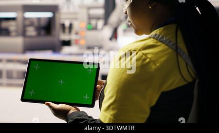 Smart factory specialist using green screen tablet to test automated systems to ensure reliability. Industry 4.0 plant technician using chroma key device to identify bottlenecks and optimize, camera B Stock Photo