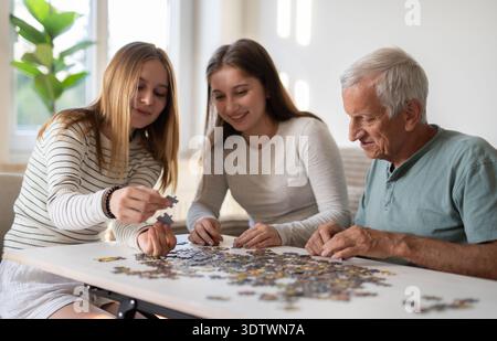 Sisters And Grandpa Having Fun, Connecting A Puzzle And Laughing Together Stock Photo