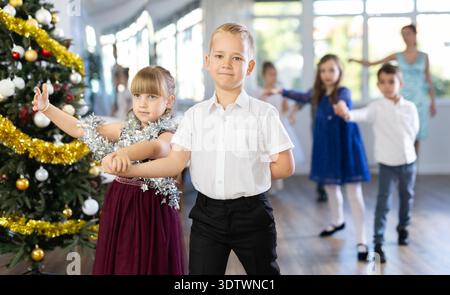 Preteen children in elegant outfits practicing partner dance in Christmas studio Stock Photo