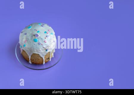 Easter cake topped with glossy icing and decorative sugar drops on vibrant purple background, festive spring dessert concept Stock Photo