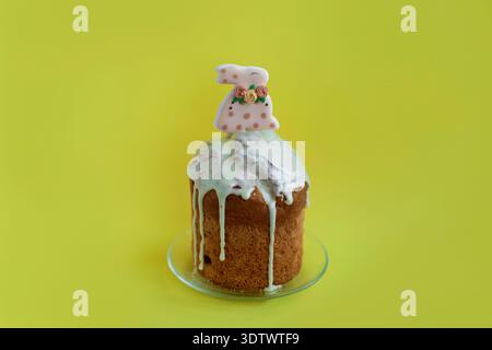 Bright Easter cake topped with white icing and bunny decoration on yellow background, cheerful spring celebration concept Stock Photo