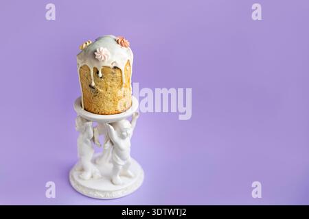 Traditional Easter cake with icing displayed on decorative white ceramic stand with angel details, soft lavender background creating elegant festive a Stock Photo