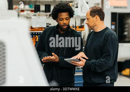 Male workers discussing with each other on tablet PC in factory Stock Photo