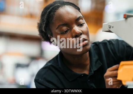 Focused young female engineer working on machine parts in factory Stock Photo