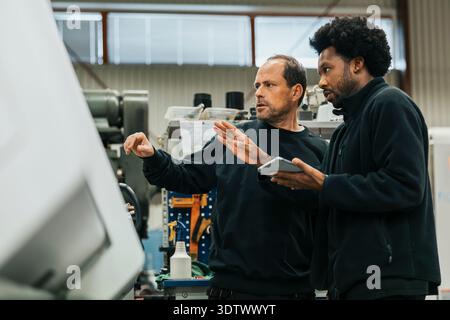 Multiracial male workers examining machine while working in factory plant Stock Photo