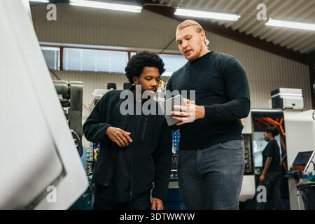 Young male worker discussing with coworker on digital tablet while working in factory Stock Photo
