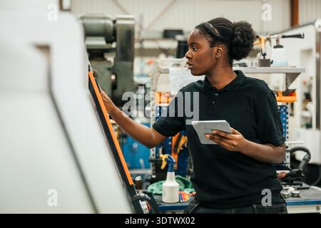 Young female worker holding tablet PC operating machine in factory Stock Photo