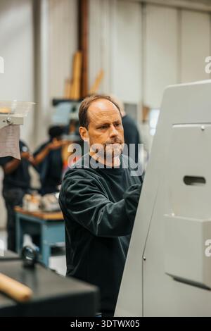 Mature male worker operating machine in factory Stock Photo