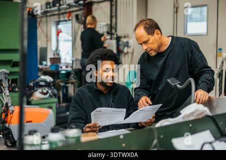 Multiracial male workers discussing instructions on paper before manufacturing products in factory Stock Photo