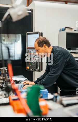 Mature male factory worker working on laptop at table Stock Photo