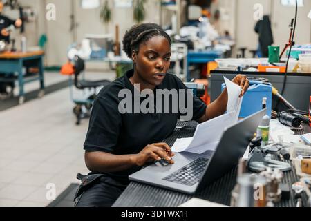Concentrated female blue-collar worker working on laptop in manufacturing industry Stock Photo