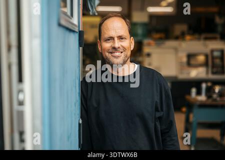 Portrait of smiling mature male worker standing near factory door Stock Photo