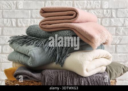 Wicker basket with cozy blankets near white brick wall, closeup Stock Photo