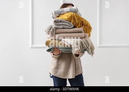 Woman with stack of plaids near light wall Stock Photo