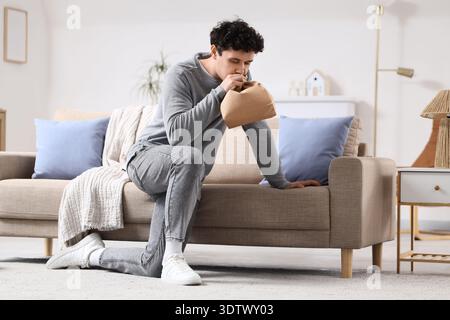 Young man with paper bag having panic attack at home Stock Photo