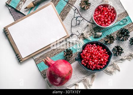 A vibrant display of pomegranate fruits and seeds arranged alongside an open notebook and pencil, all set on a textured textile surface surrounded by Stock Photo